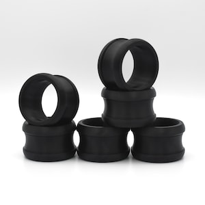 May include: Five black rubber rings stacked on top of each other. The rings are all the same size and shape, and they have a smooth, glossy finish.