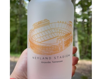 May include: A frosted glass with a gold outline of Neyland Stadium, home of the University of Tennessee Volunteers football team, in Knoxville, Tennessee. The text "Neyland Stadium Knoxville, Tennessee" is printed on the glass.