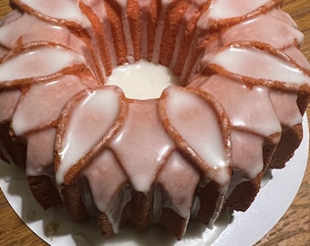 May include: A pink and white bundt cake with a white glaze. The cake is decorated with a flower design.