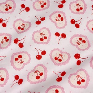 May include: White fabric with a repeating pattern of red cherries and pink hearts. The hearts have a scalloped edge and a bow detail. Small star shapes are scattered across the background.