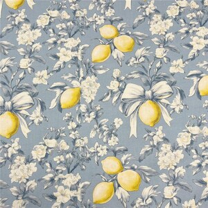 May include: A repeating pattern of lemons, white flowers, and bows on a light blue background. The lemons are yellow, and the flowers and bows are white. The leaves and stems are a muted gray-blue. This design is suitable for fabric or wallpaper.
