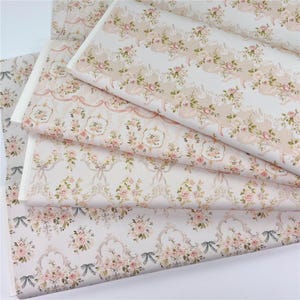 Puede incluir: Varias hojas de papel con estampado floral. El papel presenta un diseño repetitivo de rosas rosas, hojas verdes y cintas sobre un fondo blanco. El papel tiene una estética vintage y romántica.