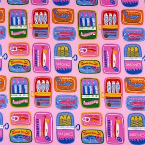 Pode incluir: Tecido rosa com um padrão repetido de latas de sardinhas coloridas. As latas apresentam ilustrações de peixes e texto em vários idiomas, incluindo "Sardines" e "Português". As latas são em tons de rosa, azul, laranja e verde.
