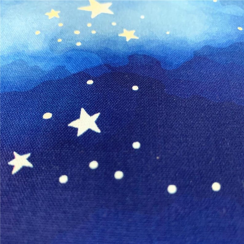 Op de afbeelding: Een close-up van een blauwe stof met een witte aquarelverloop en witte sterren en stippen erop gedrukt.