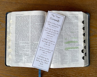 May include: A white bookmark with black text outlining temple covenants. The bookmark includes a list of covenants and scriptures. The bookmark is placed on an open Bible with the text of the Book of Mormon.