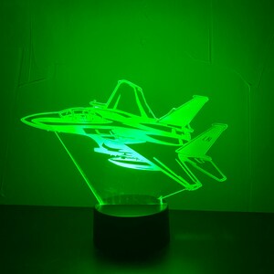 May include: A green LED night light shaped like a jet airplane with the letters "LN" on the tail. The night light is on a black base.