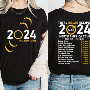 Peut inclure: T-shirt noir avec un graphique d'une éclipse solaire et le texte "2024 Eclipse solaire totale". Le dos du t-shirt présente une liste de villes et d'heures pour l'éclipse solaire totale de 2024.