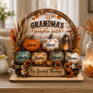 May include: A decorative wooden display featuring the text "GRANDMA'S pumpkin patch" and "Our Greatest Blessings." It includes six pumpkins in orange, white, and blue, each personalized with names, accented by wheat stalks, sunflowers, and a lantern.