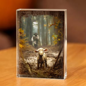May include: A clear acrylic block featuring a pastoral scene. A lamb stands in muddy terrain, with a person walking in the background. The scene is framed by a wooden border and autumn foliage.