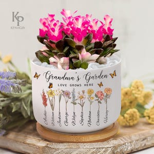 May include: White ceramic planter with the text "Grandma's Garden Love Grows Here" and a floral design with butterflies. The planter has a bamboo base and features names of family members around the bottom.
