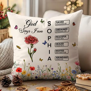 May include: Cream-colored decorative pillow with floral and butterfly accents. The pillow features the text "God Says I Am" and the name "Sophia" spelled out vertically. Additional text includes Bible verses.