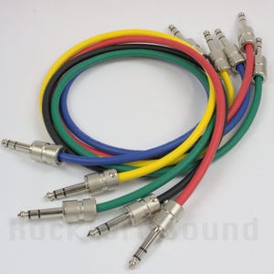 May include: A collection of multi-colored audio cables with silver-colored connectors. The cables are red, yellow, green, black, and blue. The cables are coiled and arranged in a circular pattern.