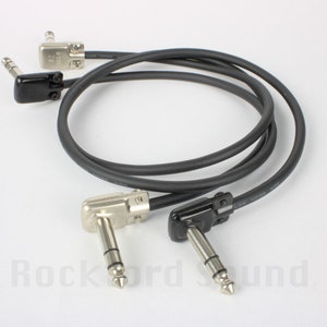 May include: Two black and silver right-angle guitar cables with low noise wire. The cables are coiled together.