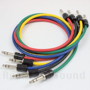 May include: A collection of six audio cables with 1/4-inch (6.35 mm) male connectors. The cables are in a variety of colors, including red, yellow, green, blue, and black. The cables are coiled and arranged in a circular pattern.