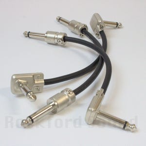 May include: Several black instrument cable patch cords with silver-colored connectors. The cables have straight and angled plugs. The cords are designed for connecting musical instruments and audio equipment.
