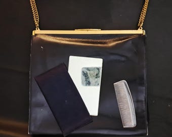 May include: A black vintage handbag with a gold chain strap, a white compact with a patterned design, a navy blue case, and a clear comb. The handbag is rectangular and has a gold clasp.