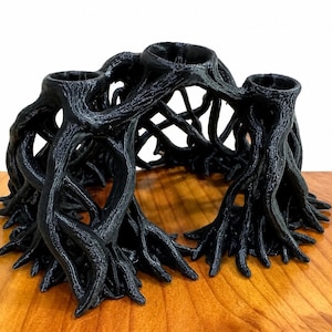 May include: A black candle holder featuring a complex, interconnected structure that mimics the appearance of tangled tree roots. The design includes three circular openings at the top for candles, supported by a network of textured, root-like branches.