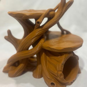 Puede incluir: Un soporte de exhibici&oacute;n de color marr&oacute;n con varios niveles, dise&ntilde;ado para parecerse a un tronco de &aacute;rbol con ramas entrelazadas y dos plataformas circulares planas. La estructura presenta una abertura hueca en forma de t&uacute;nel en la base.