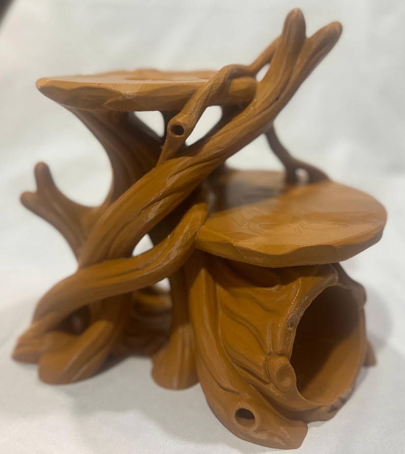 Puede incluir: Un soporte de exhibici&oacute;n de color marr&oacute;n con varios niveles, dise&ntilde;ado para parecerse a un tronco de &aacute;rbol con ramas entrelazadas y dos plataformas circulares planas. La estructura presenta una abertura hueca en forma de t&uacute;nel en la base.