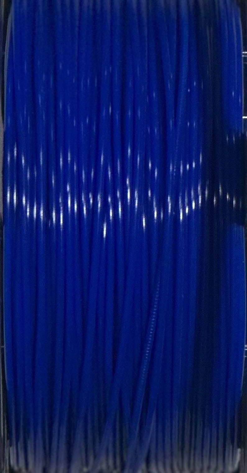 Puede incluir: Una bobina de filamento para impresora 3D de color azul real vibrante, enrollada firmemente en una espiral continua y suave. El material pl&aacute;stico transl&uacute;cido refleja la luz a lo largo de su longitud vertical, mostrando una forma cil&iacute;ndrica uniforme.