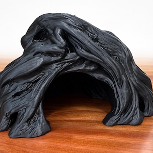 May include: A matte black, hollow, cave-like structure with a textured, organic surface that mimics the appearance of flowing, layered material. The object features a wide, arched opening at the front and a solid, irregular exterior form.