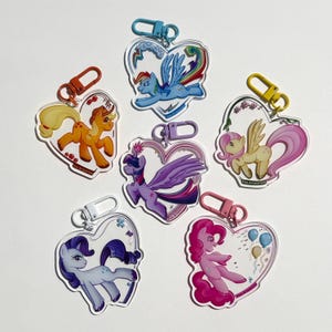 May include: Six heart-shaped acrylic keyrings featuring cartoon pony characters in various colours. Each keyring has a different pony design with a matching coloured clasp. The keyrings are displayed on a white background.