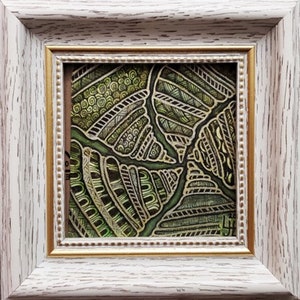 May include: A framed artwork featuring a green and gold abstract design with intricate patterns and swirls. The artwork is framed in a white frame with a gold inner border.