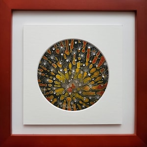 Puede incluir: Una obra de arte circular enmarcada con un fondo negro y un diseño colorido de amarillo, naranja y rojo. El diseño presenta un patrón radial de líneas y puntos, con pequeños diamantes de imitación blancos dispersos.
