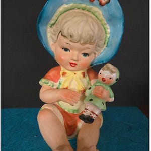 Vintage Piano Baby Bisque Porcelain Peach and Blue 7” Little Girl with Doll by Lipper & Mann, Japan. 30 Dollars. OPDC-0134