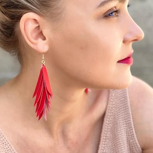 以下が含まれることがあります： 金色のフックが付いた赤い羽根型のイヤリング。イヤリングは、重ねられた赤い素材で作られており、滝のような効果を生み出しています。大胆なアクセサリーで、彩りを添えます。