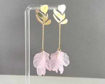 May include: Gold-toned leaf-shaped earrings with a delicate chain and cascading pink petal accents. These dangle earrings are a stylish accessory, perfect for adding a touch of elegance to any outfit. The earrings are displayed on a clear stand.