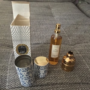 May include: A set of perfume bottles and a box with a black and white geometric pattern. The bottles are gold and clear with a gold cap. The box has the text "spray eau de toilette Chamade Guerlain" on it.