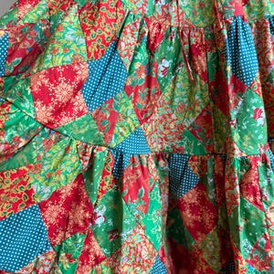 Puede incluir: Prenda de tela de retazos con una vibrante mezcla de telas rojas, verdes y turquesas. El dise&ntilde;o incorpora varios patrones, incluyendo estampados florales, lunares y motivos festivos navide&ntilde;os. La prenda tiene una construcci&oacute;n escalonada con un dobladillo con volantes.
