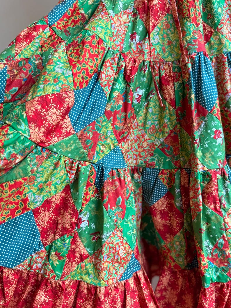 Puede incluir: Prenda de tela de retazos con una vibrante mezcla de telas rojas, verdes y turquesas. El dise&ntilde;o incorpora varios patrones, incluyendo estampados florales, lunares y motivos festivos navide&ntilde;os. La prenda tiene una construcci&oacute;n escalonada con un dobladillo con volantes.
