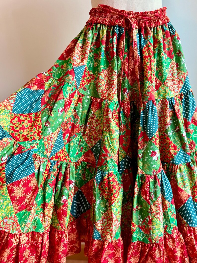 Puede incluir: Falda patchwork con tem&aacute;tica navide&ntilde;a. La falda presenta un dise&ntilde;o escalonado con paneles rojos, verdes y turquesas. La tela tiene estampados florales y de lunares. La cintura es roja con un cord&oacute;n.