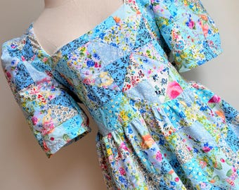 May include: A blue and white patchwork dress with a square neckline and short puff sleeves. The dress has a floral print and is made of cotton.