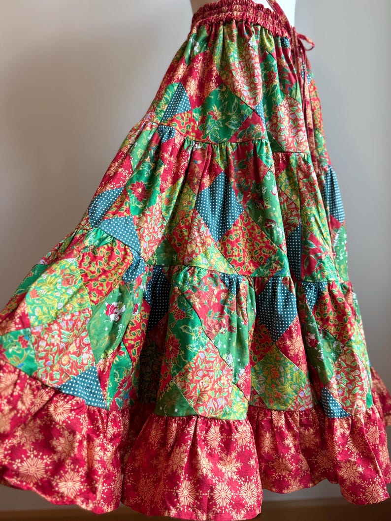 Puede incluir: Falda patchwork escalonada en rojo, verde y turquesa. La falda presenta estampados florales y de lunares. Tiene un dobladillo con volantes y una cintura con cord&oacute;n. La longitud de la falda es de aproximadamente 90 cm.