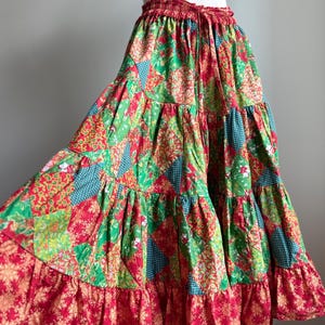 Puede incluir: Falda de patchwork escalonada en tonos rojos, verdes y azules. La falda presenta una cintura con cord&oacute;n y un dobladillo con volantes. La tela tiene estampados florales y geom&eacute;tricos, creando una est&eacute;tica bohemia vibrante.
