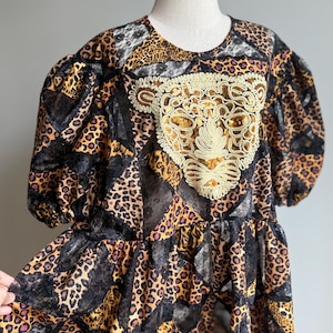 May include: A leopard print dress with a round neckline and short, puffy sleeves. The dress features a gold sequined applique on the bodice and black lace accents. The dress is displayed on a mannequin.