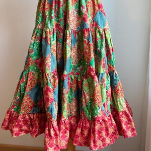 Puede incluir: Falda patchwork escalonada con cintura el&aacute;stica roja. Presenta telas verdes, rojas y turquesas con estampados florales y de lunares. El dobladillo inferior tiene un volante rojo con un dise&ntilde;o floral dorado.
