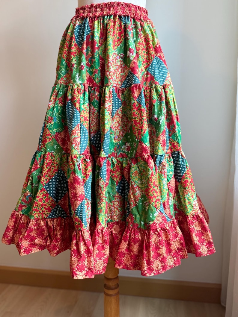 Puede incluir: Falda patchwork escalonada con cintura el&aacute;stica roja. Presenta telas verdes, rojas y turquesas con estampados florales y de lunares. El dobladillo inferior tiene un volante rojo con un dise&ntilde;o floral dorado.