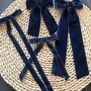 May include: Four navy blue velvet hair bows with long tails. The bows are arranged on a woven straw surface.