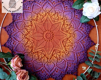 May include: A handmade, crocheted doily in a starburst pattern, featuring a gradient of colors from orange to purple. The doily is displayed on a white hoop, with the "Crochet Frog Pattern Designer" logo in the upper left corner. Roses and greenery surround the doily.