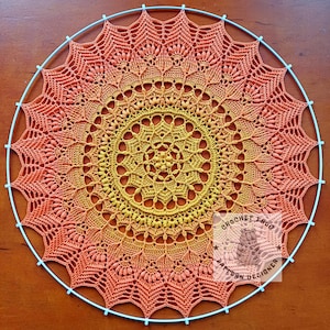 May include: A large, round, crocheted mandala in shades of orange, yellow, and red. The mandala is hanging on a blue metal hoop.