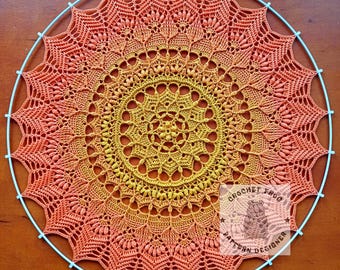 Puede incluir: Un gran mandala redondo tejido a crochet en tonos naranja, amarillo y rojo. El mandala está colgado en un aro de metal azul.