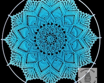 May include: A turquoise crochet mandala, featuring intricate patterns and a central floral design. The mandala is suspended within a white metal hoop. The image includes the text "Crochet Frog Pattern Designer".