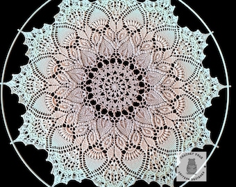 May include: A cream-colored, circular crochet doily with a detailed floral pattern. The doily is mounted within a white metal ring. The design features intricate lace-like details and a gradient of color from the center to the edges. The image is set against a black background.