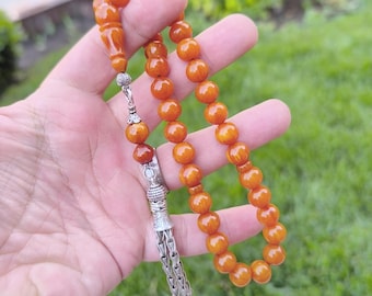 May include: A brown amber prayer beads necklace with a silver tassel. The beads are round and have a smooth, polished finish.