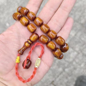 Op de afbeelding: Een bruine houten gebedsketting met een gouden kwast en een gouden label met de tekst "ABDO".