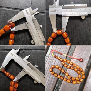 Op de afbeelding: Een set amberkleurige houten gebedskralen met een rode kwast. De kralen worden gemeten met een schuifmaat, wat aangeeft dat de grootte van elke kraal ongeveer 3,8 cm in diameter is.